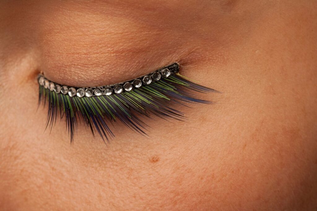 pexels photo 12585802 A striking close-up of eyelashes with colorful feathers and rhinestones, showcasing detailed fashion makeup artistry.