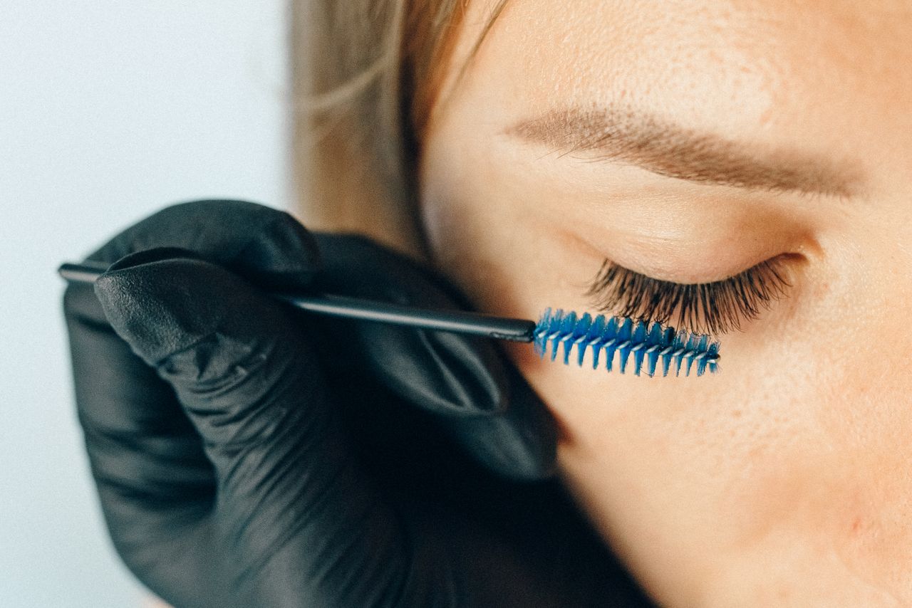 Usługi A professional applying eyelash extensions using a blue applicator brush for a refined look.