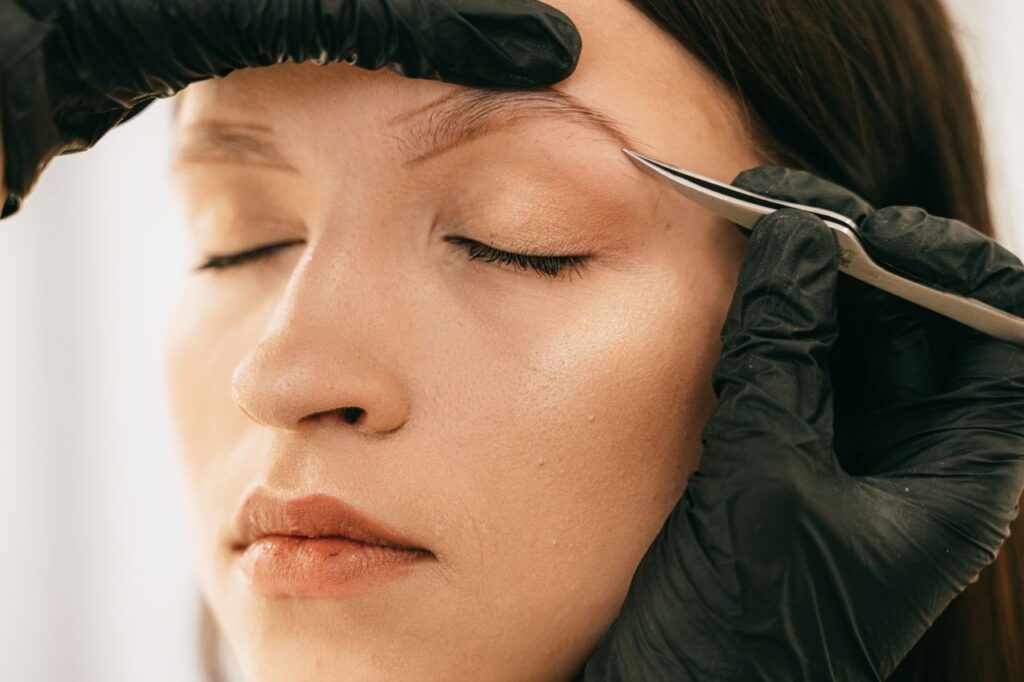 pexels photo 5177994 5177994 Detailed image of woman getting eyebrows plucked with tweezers by a beautician wearing gloves.